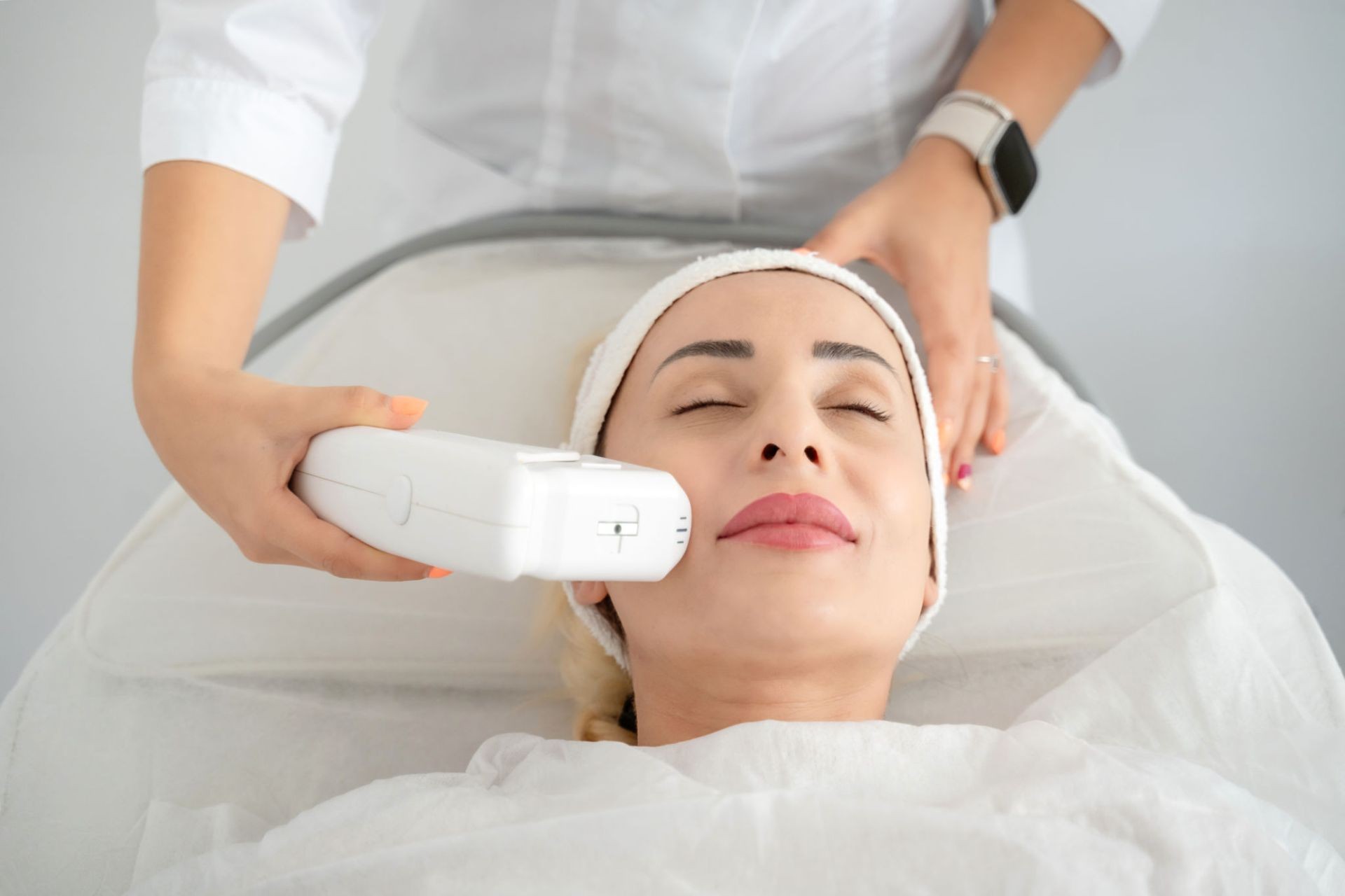 Person receiving a facial treatment with a handheld device in a spa or clinic setting.